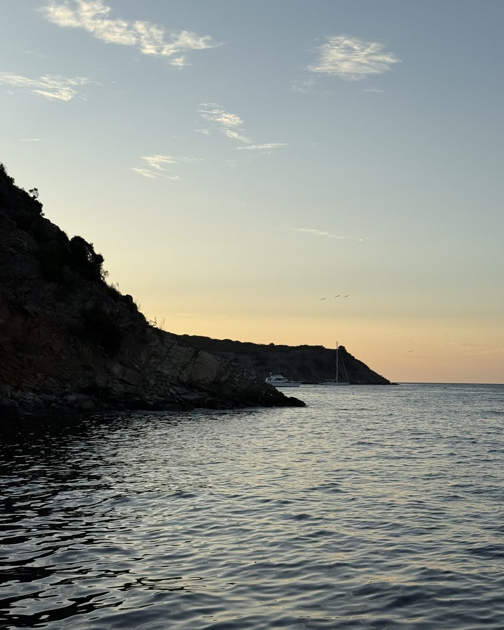 The Southern California coast at Catalina Island at dusk, a sailboat anchored off the point.